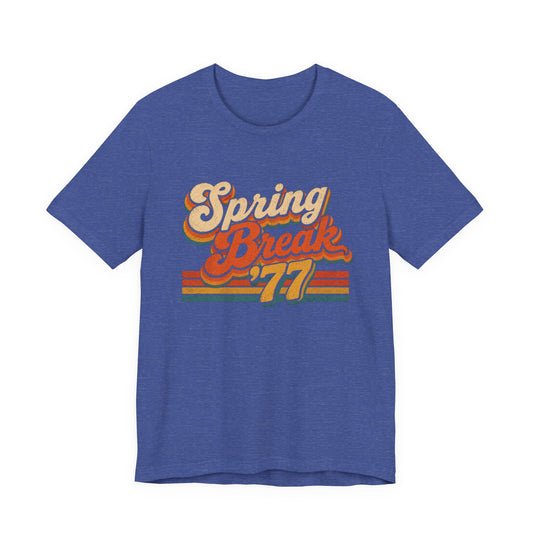 A heather blue short-sleeve t-shirt with a retro-style graphic on the chest reading 'Spring Break '77' in cream, orange, and yellow.