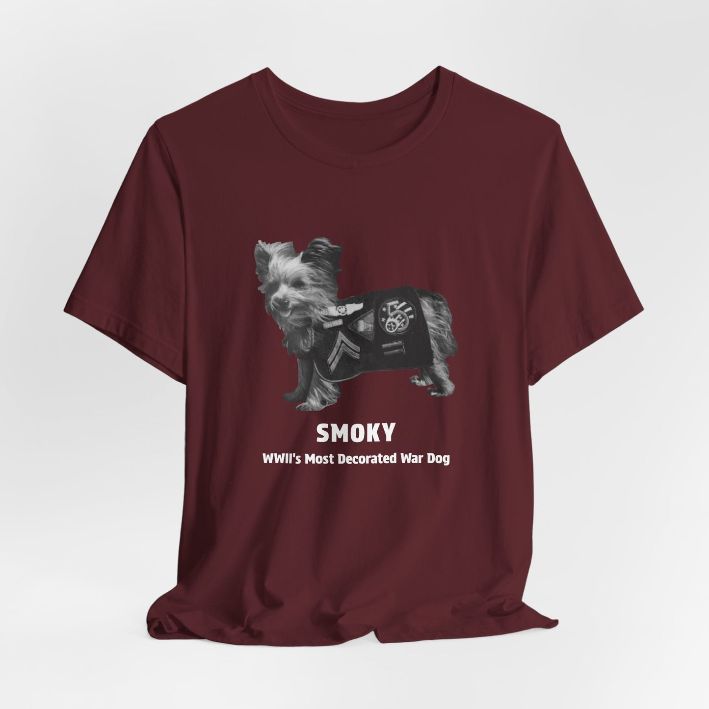 A maroon short-sleeve t-shirt with a graphic of a small dog and the text 'SMOKY WWII'S Most Decorated War Dog' printed on the front.