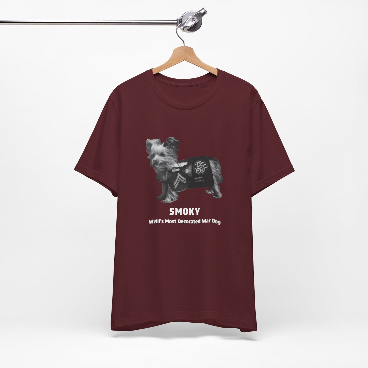 A maroon short-sleeve t-shirt featuring a black and white graphic of a dog wearing a military vest with the text 'SMOKY' and 'WII'S MOST Decorated War Dog' printed below.