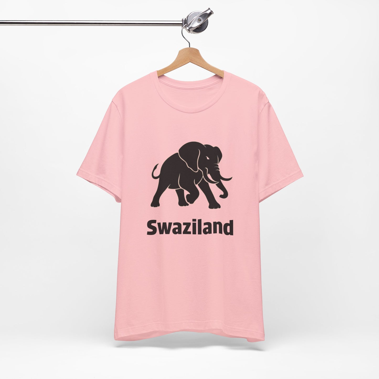 A light pink short-sleeve t-shirt features a black graphic of a walking elephant with the word 'Swaziland' printed underneath in a bold black font.