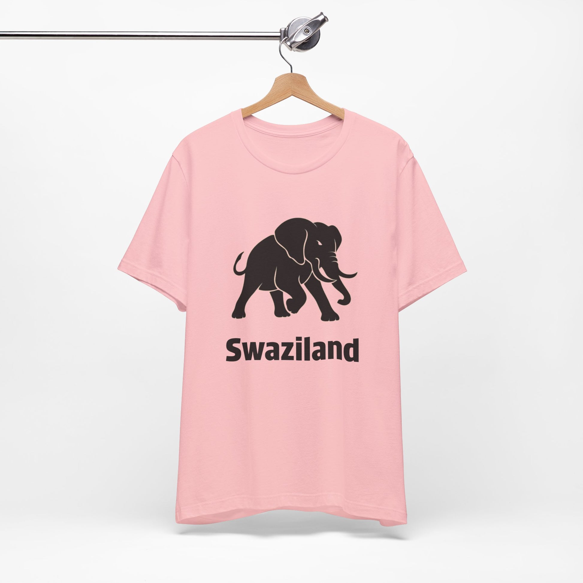 A light pink short-sleeve t-shirt features a black graphic of a walking elephant with the word 'Swaziland' printed underneath in a bold black font.