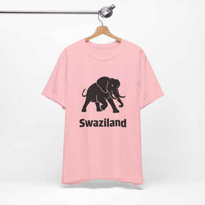 A light pink short-sleeve t-shirt features a black graphic of a walking elephant with the word 'Swaziland' printed underneath in a bold black font.